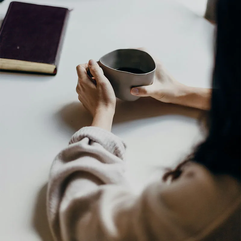 Hands resting around a mug beside an unopened notebook